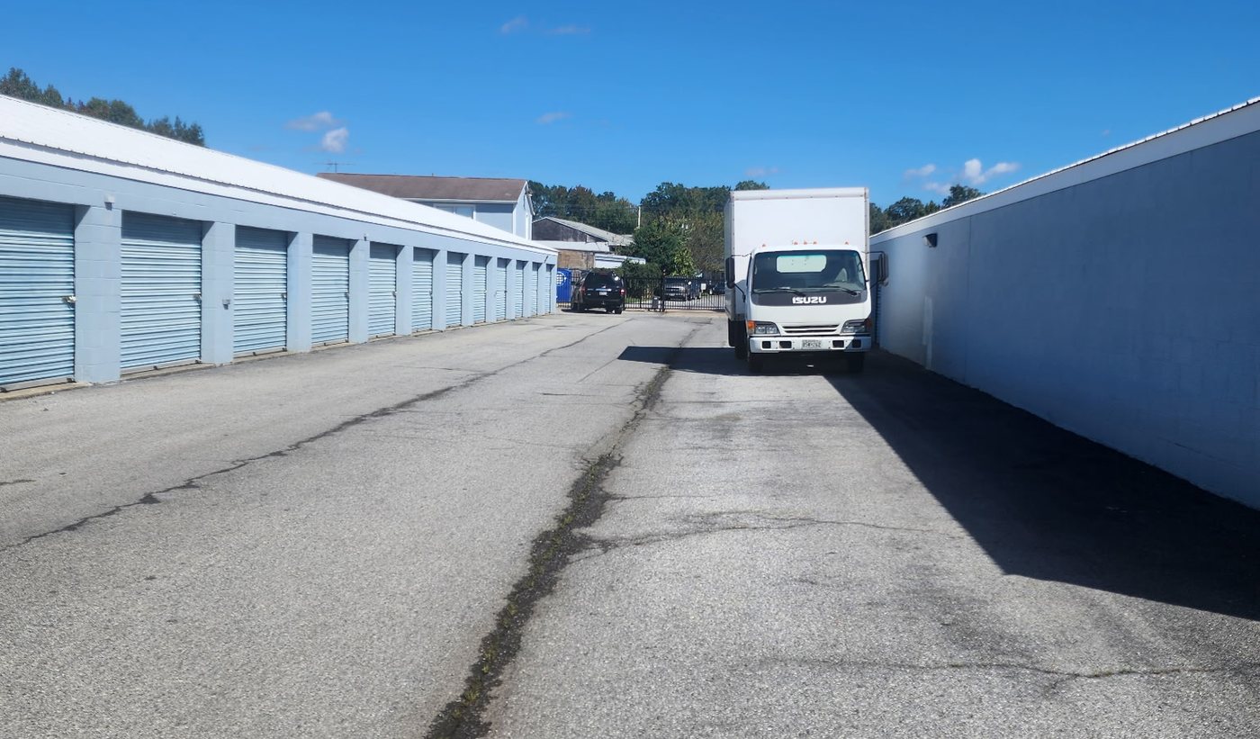 Box truck parked beside a wide drive aisle of drive-up storage units at Economy Storage in Waldorf, MD, with perimeter fencing and the security gate at the far end